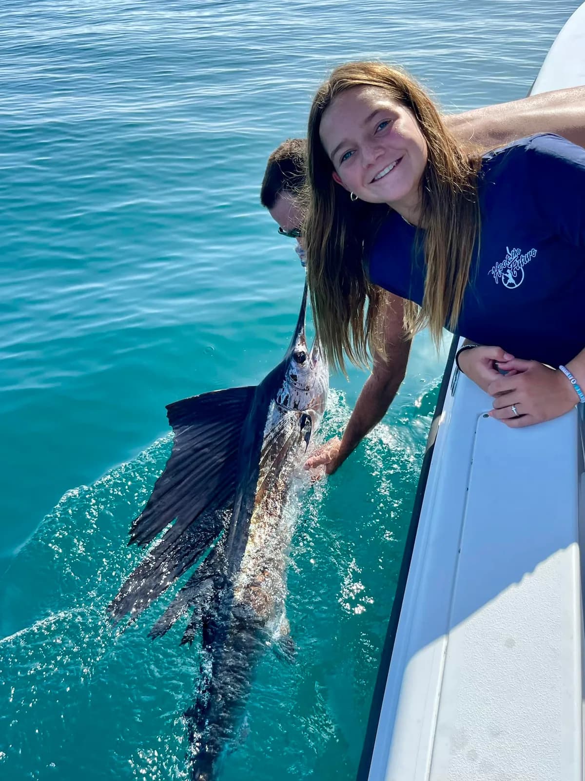 Young angler gently releasing a sailfish over the side of the boat in clear water