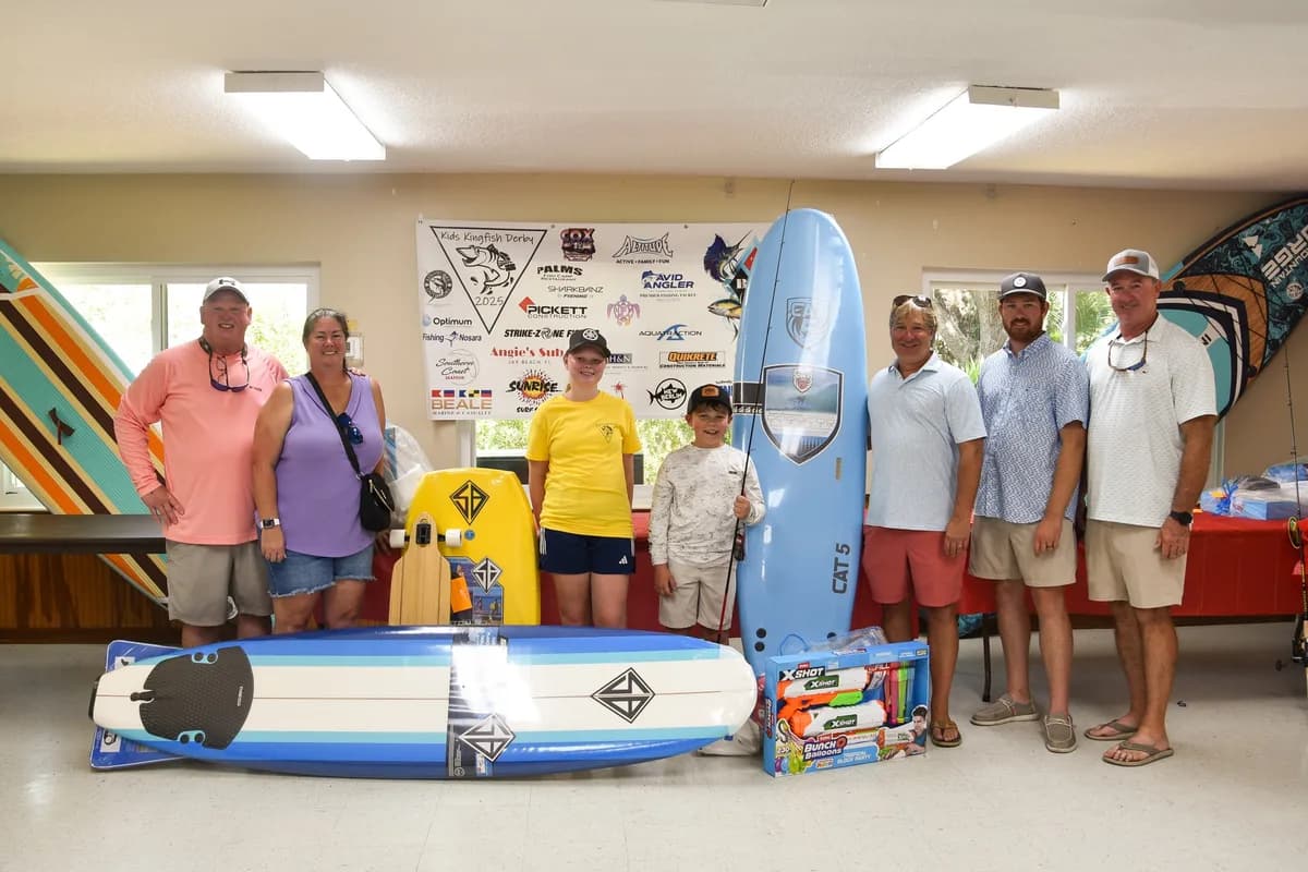 Group of parents and young anglers at the awards ceremony surrounded by paddleboards and other prizes