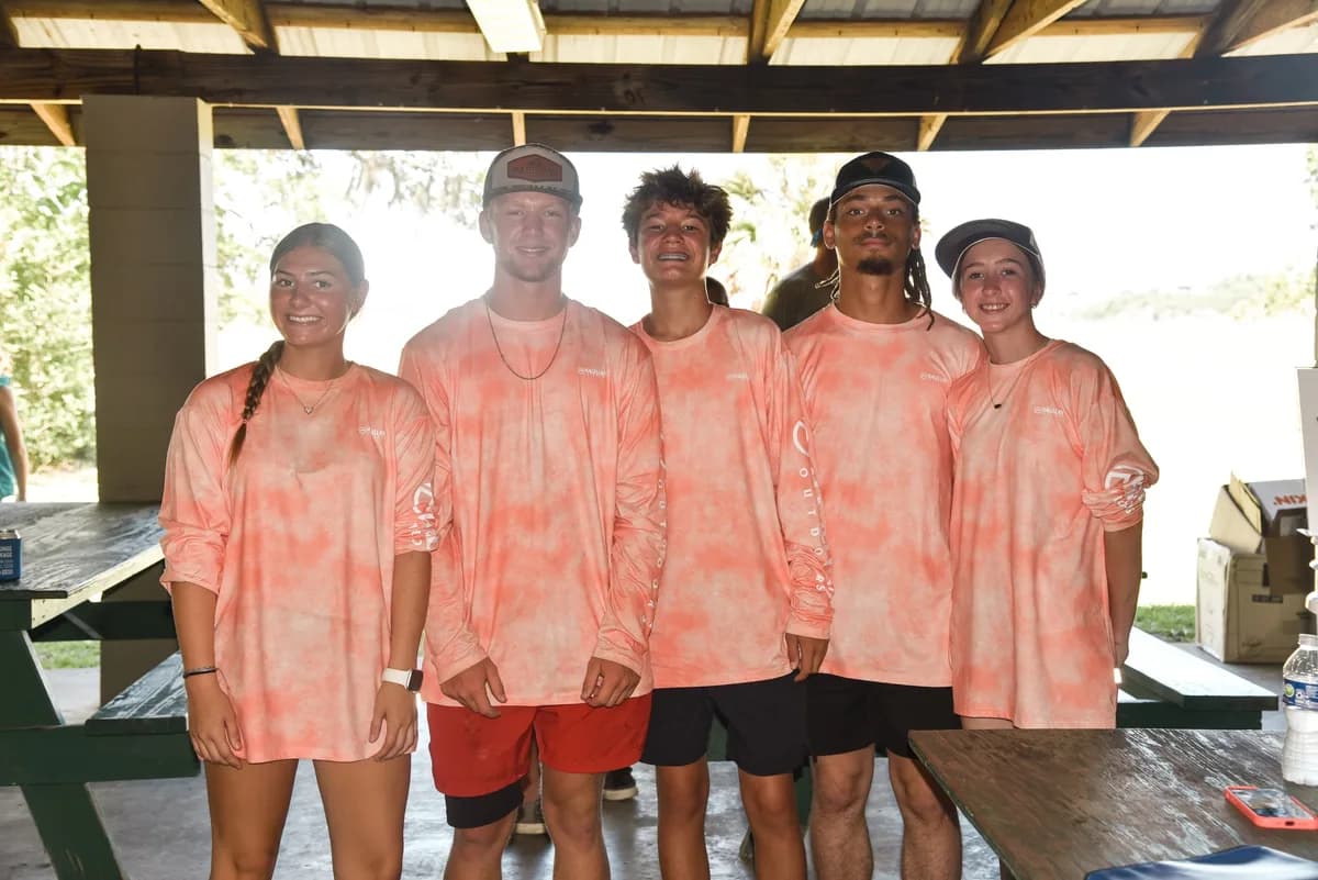 Five teen volunteers wearing matching salmon-colored tournament shirts smiling together at the awards cookout