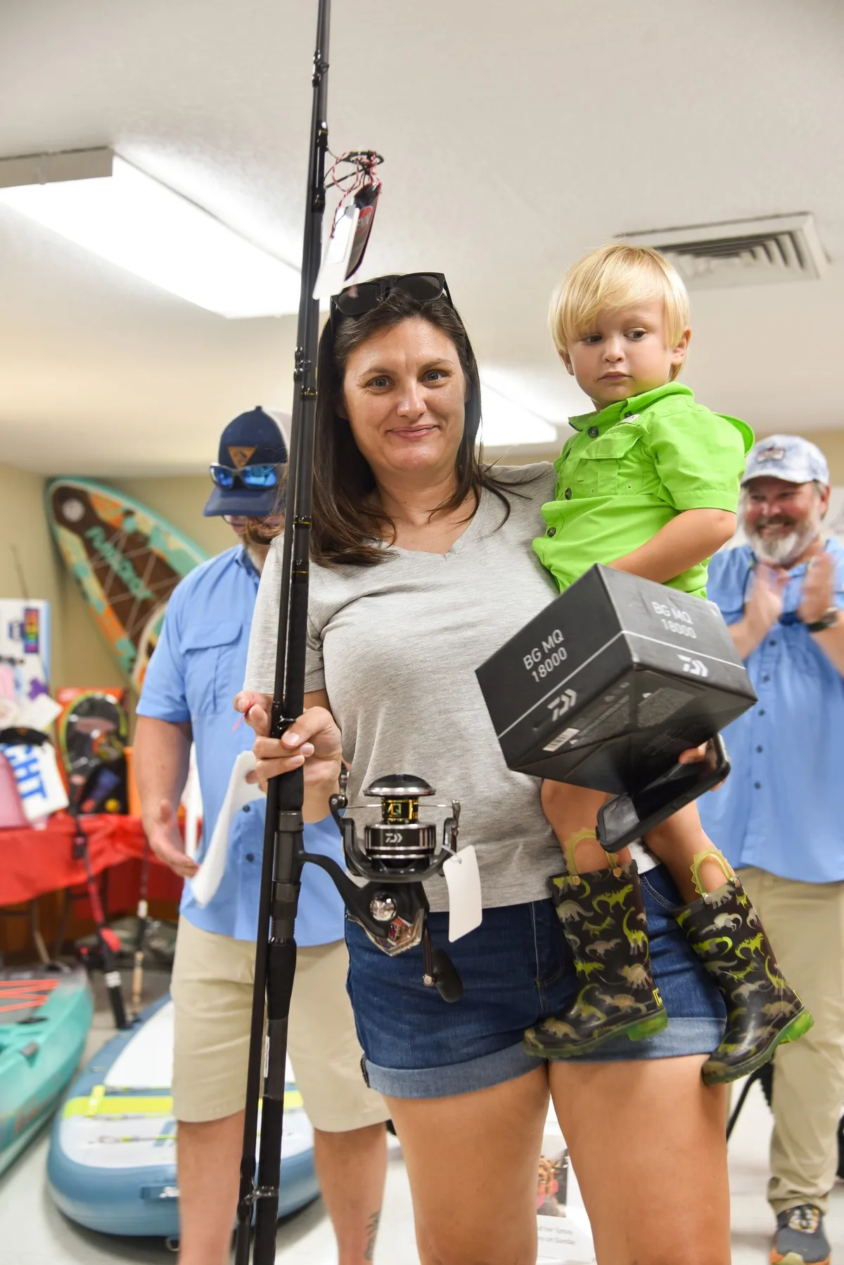 Woman holding a Daiwa fishing rod and reel prize while carrying a young boy at the Kids Kingfish Derby awards