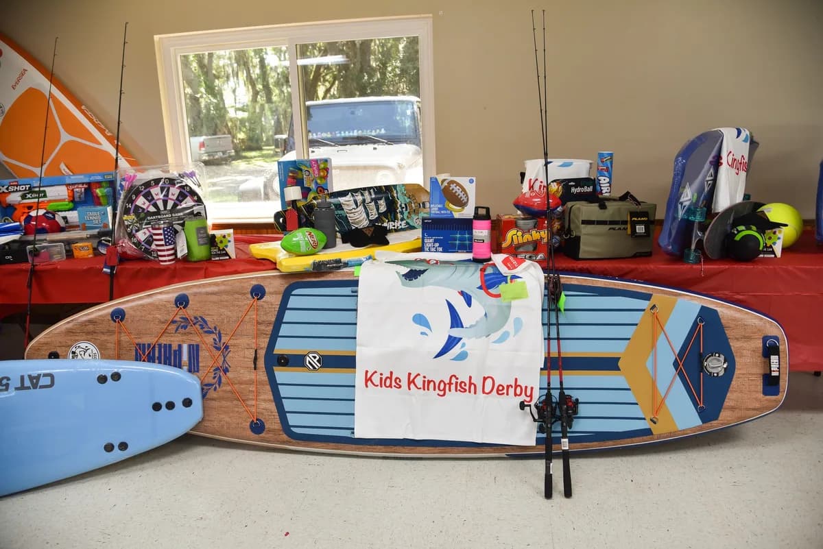 Kids Kingfish Derby branded stand-up paddleboard displayed with fishing rods and other prizes at the awards event